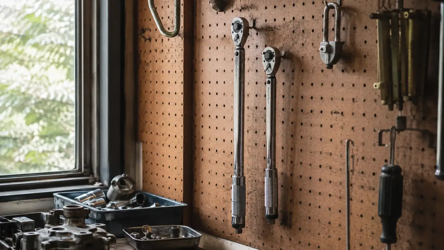 A torque wrench hung on a wall pegboard above a workbench with a drivetrain strewn across it