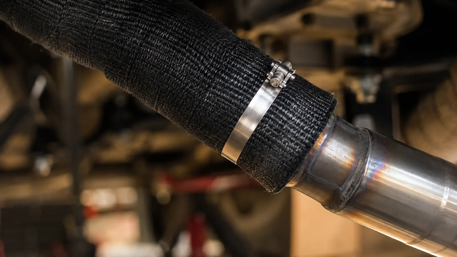 A close-up of a wrapped motorcycle exhaust header with a stainless steel tie clamped at the end of the wrap